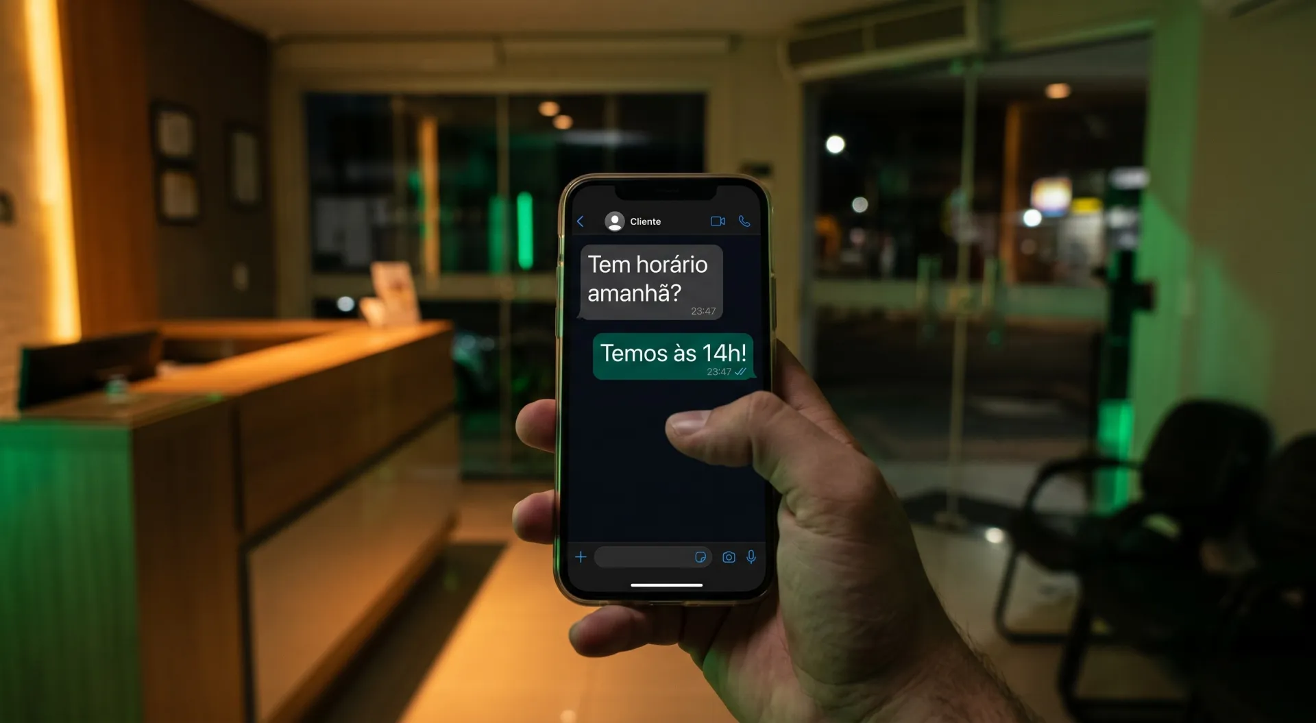 Mão segurando o celular à noite na recepção fechada, com o cliente perguntando às 23:47 se tem horário amanhã e a resposta chegando na hora